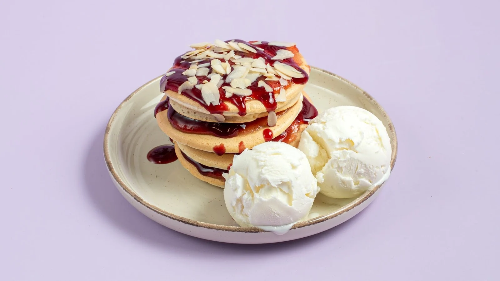 Pancakes with berry sauce, almonds and scoops of Aega's goat's-milk ice cream on a plate, Thessaloniki