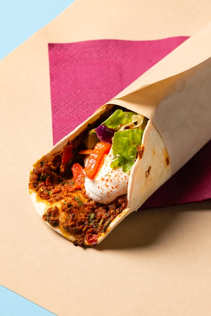 A Levantine spiced-meat wrap in paper on a pink napkin at Feyrouz, Thessaloniki