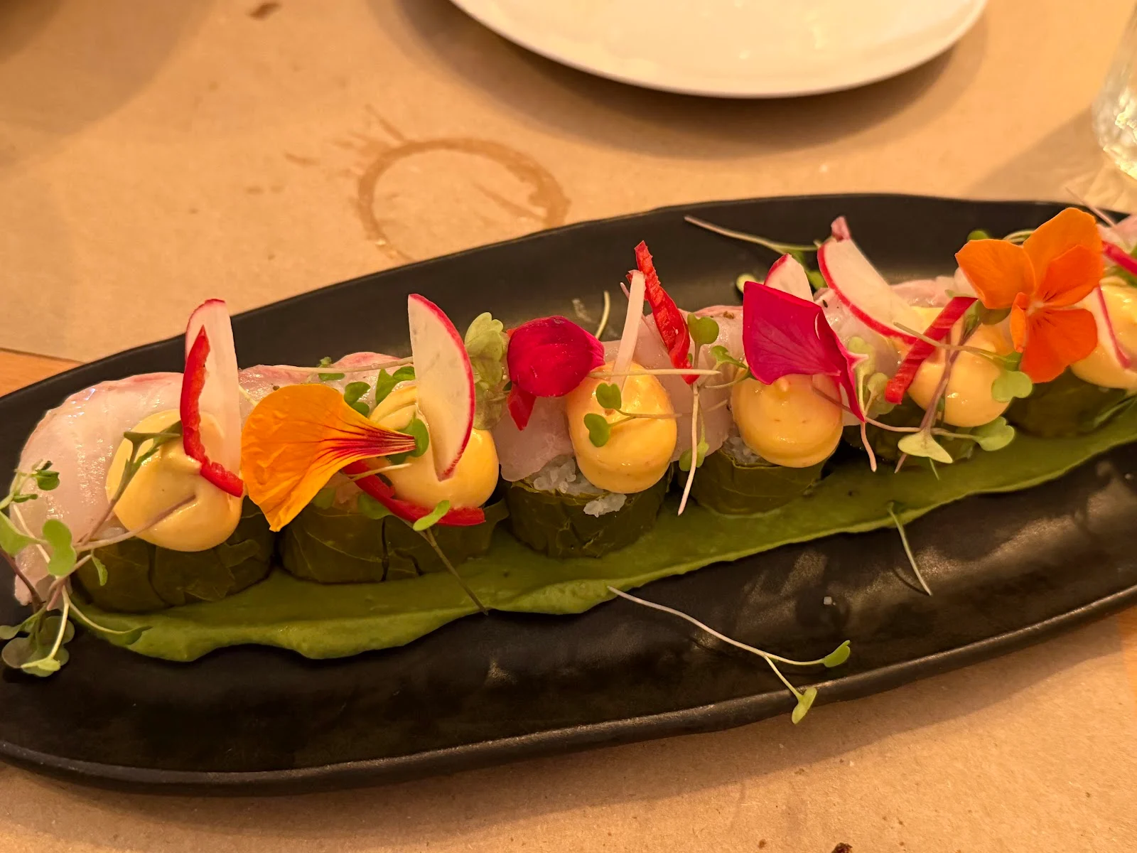 Vine-leaf 'sushi' topped with seabass and edible flowers on a long plate at Iliopetra, Thessaloniki