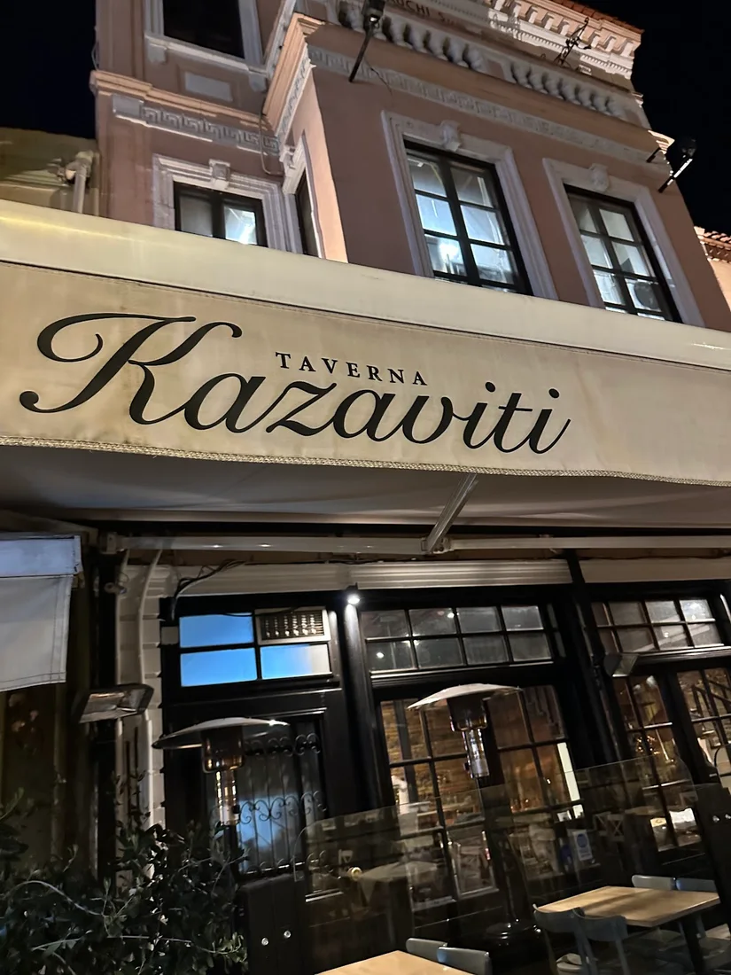 The lit night storefront of Kazaviti taverna in Ladadika, its cursive sign over the awning, Thessaloniki
