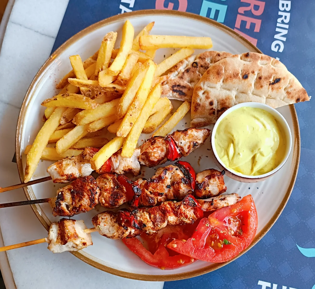 A plate of chargrilled chicken souvlaki skewers with chips, pita and a yellow dip at Savvikos on Aristotelous Square, Thessaloniki