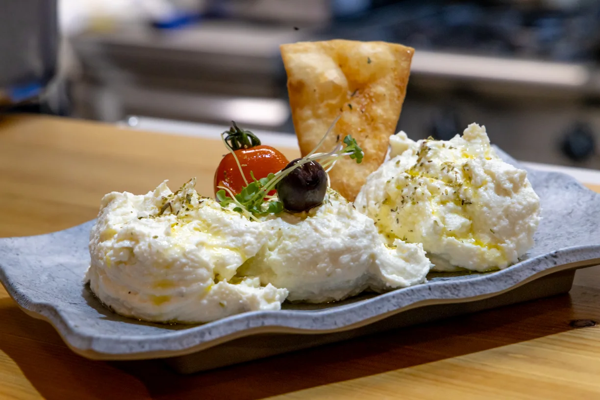 A plate of whipped feta topped with cherry tomato and olive, served with a fried-pastry cracker at Stafylos Gi, Thessaloniki