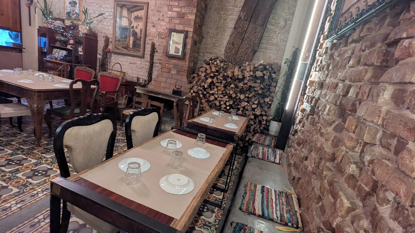 The rustic brick-walled dining room of Stou Mitsou taverna in the Vlali market — vintage chairs, set tables and stacked firewood, Thessaloniki