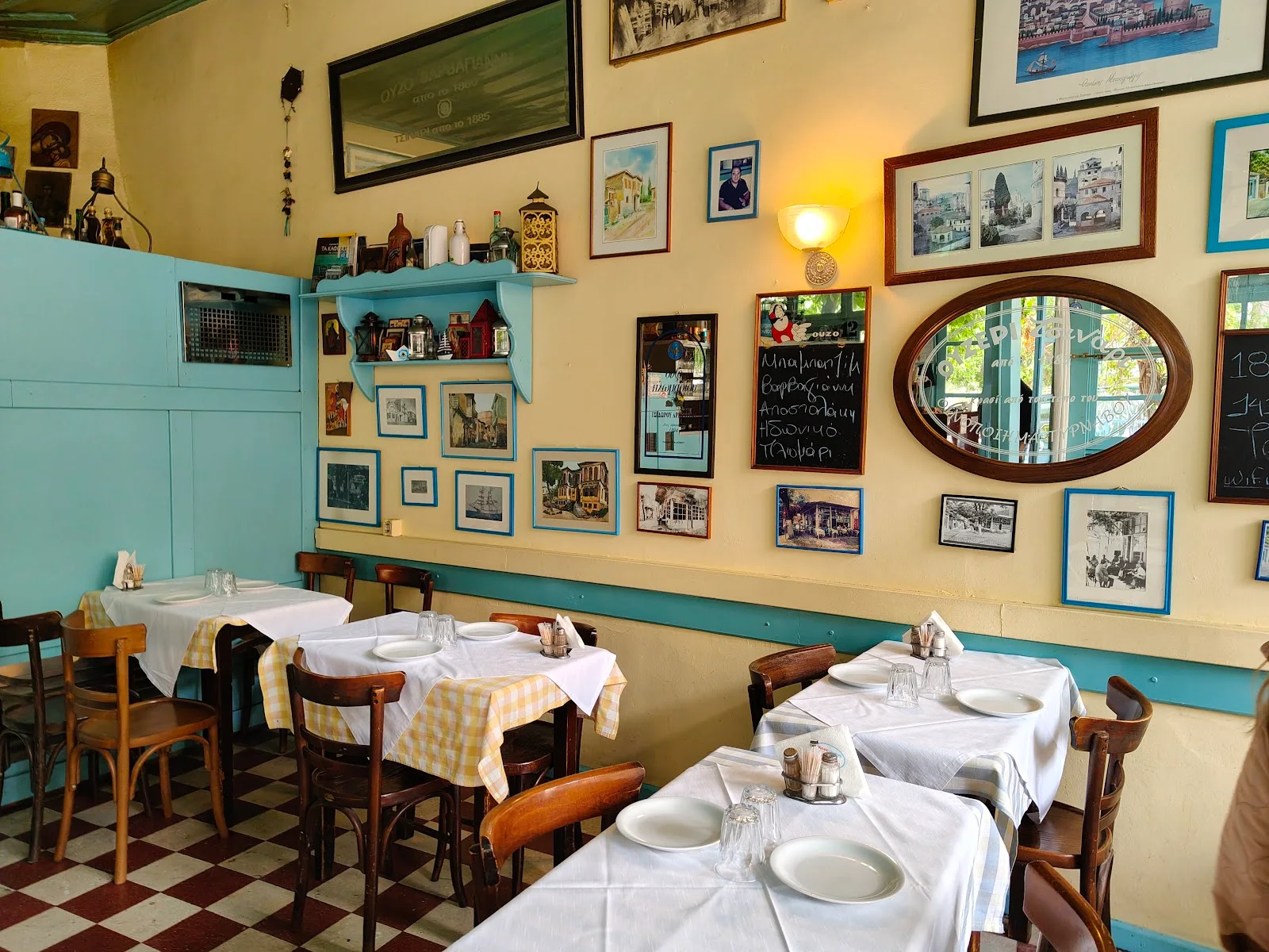 The vintage interior of Tsinari ouzeri in Ano Poli — yellow walls hung with old photographs, a checkerboard floor and gingham-clothed tables, Thessaloniki