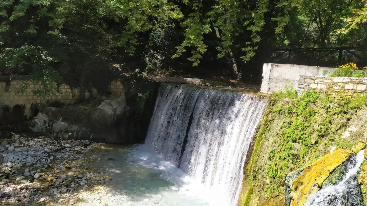 A thermal waterfall tumbling into a turquoise bathing pool at Loutra Pozar