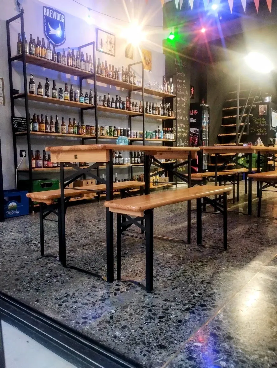 Shelves packed with craft-beer bottles behind wooden biergarten benches at Black Dog bottle shop and taproom in Thessaloniki