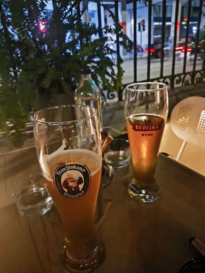 Two wheat beers on a table by the street railing at Dentro sto Bar, an all-day garden bar in eastern Thessaloniki