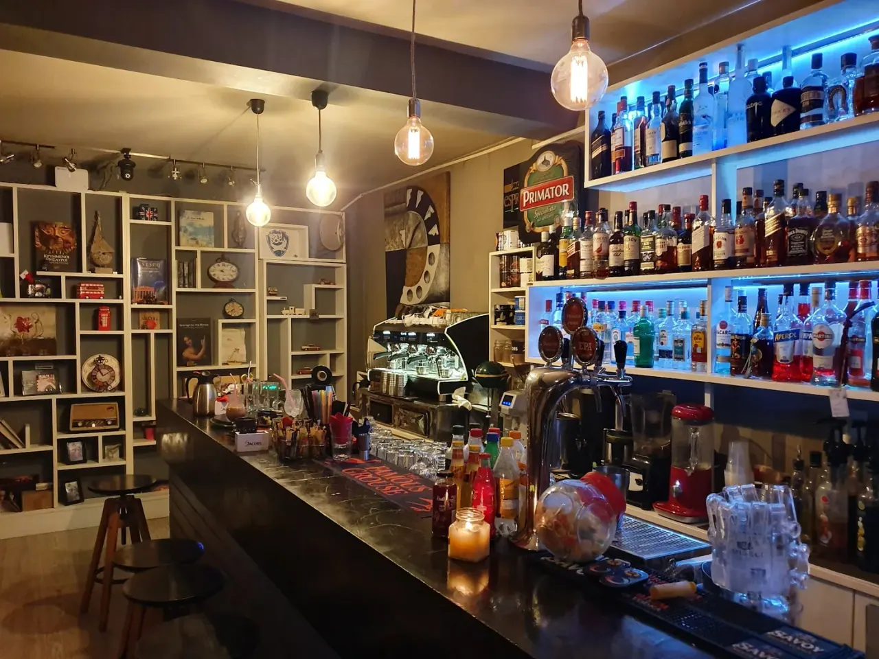 The warm, curio-filled bar of Poco Loco with backlit bottles and hanging bulbs in central Thessaloniki