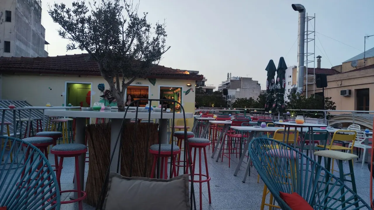 The colourful open-air rooftop terrace of Urania bar, with bright bar stools and an olive tree above the Valaoritou rooftops in Thessaloniki